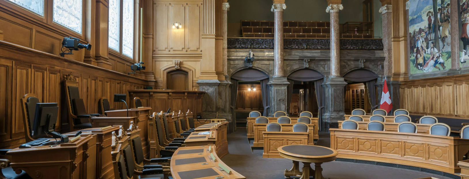 Interior of a traditional courtroom with wooden paneling, marble columns and curved rows of desks